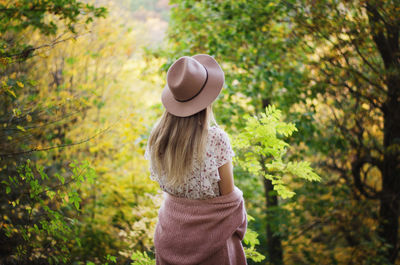 Rear view of woman wearing hat standing against plants