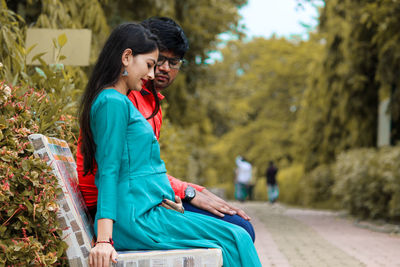 Smiling couple sitting on bench against trees