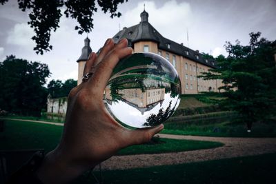 Cropped hand holding crystal ball against trees