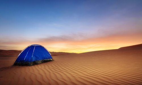 Blue tent at desert against sky during sunset