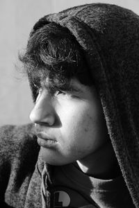 Close-up of young man wearing hoodie looking away sitting against wall