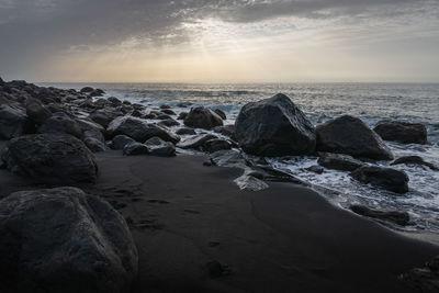 Rocks on beach against sky during sunset