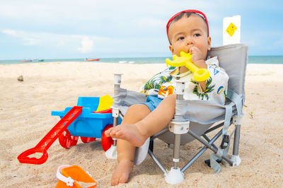 Happy boy sitting on toy at beach against sky