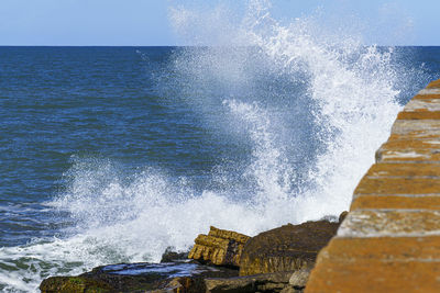 Waves splashing on rocks at sea against sky