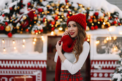 A beautiful woman with red lips in a warm hat stands by a decorated christmas van on the street