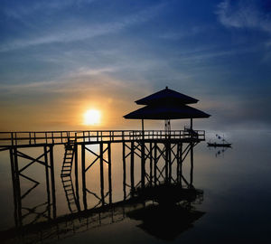 Silhouette built structure by sea against sky during sunset