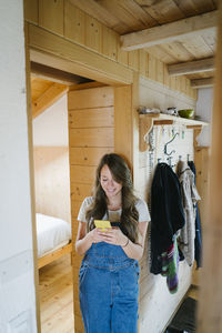 Smiling young woman using smart phone in doorway