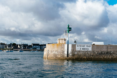 Lighthouse amidst buildings and sea against sky