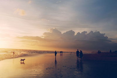 People at beach against sky during sunset