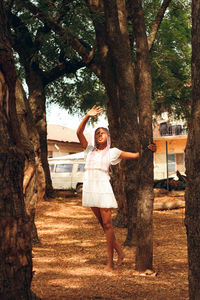 Full length of young woman looking up standing by tree trunk