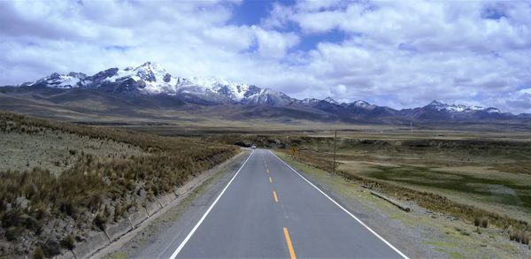 Empty road amidst landscape against cloudy sky