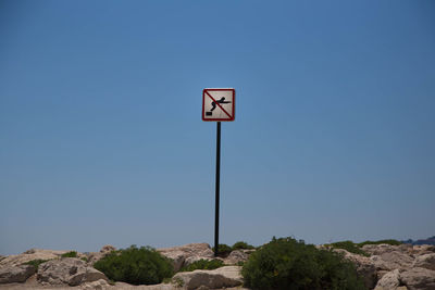 Warning sign on rocks against clear sky