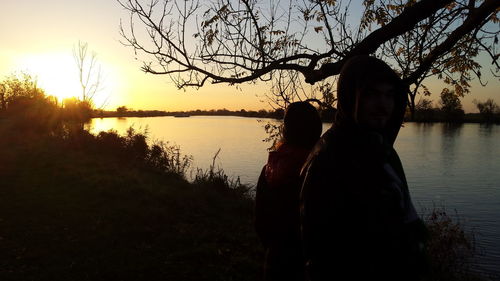 Silhouette woman standing by lake against sky during sunset