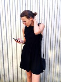 Young woman using mobile phone while standing against fence