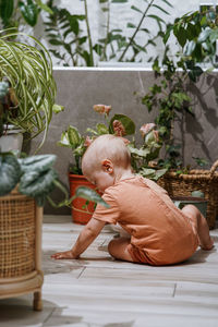 Little funny baby boy helping his mother take care for potted plants in the bathroom