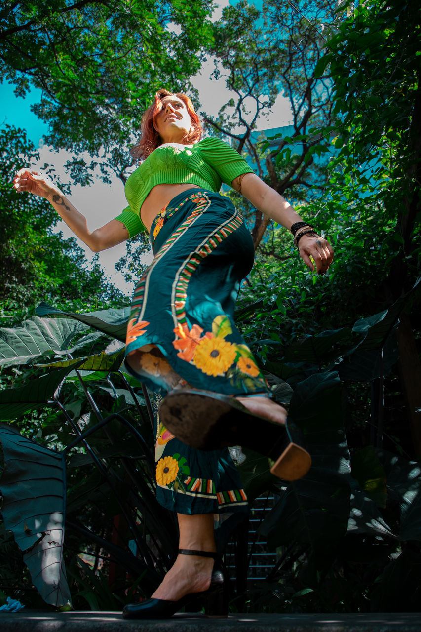 tree, plant, one person, full length, adult, green, nature, arts culture and entertainment, standing, women, outdoors, jungle, person, dancing, young adult, clothing, leisure activity, happiness, day, emotion, low angle view, lifestyles, fun