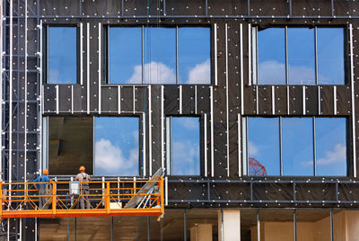 Builders install large double glazed windows on the facade of a house under construction. 