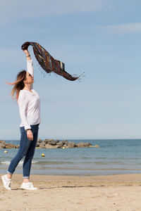 Woman waving scarf while standing on beach against sky