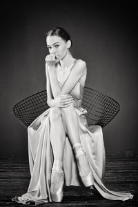 Portrait of a ballerina in a pink dress is sitting on a chair with her leg in the slit of the dress