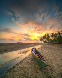 Boat moored on beach against sky during sunset