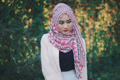 Portrait of beautiful young woman standing against plants