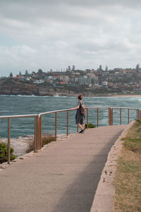 Full length of woman looking at view while standing by sea in city