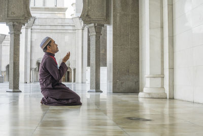 Side view of mature man praying while kneeling at mosque