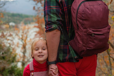 Little girl  holds the hand of her father, standing with his back, background of an autumn forest