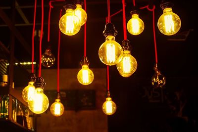 Low angle view of illuminated light bulbs hanging indoors