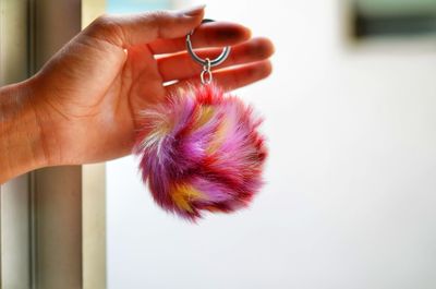 Cropped hand of woman holding fur key ring against window