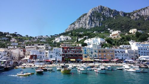 Sailboats moored in sea by town against clear sky