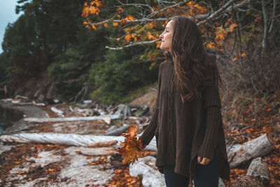 Woman holding autumn leaves while standing against trees in forest