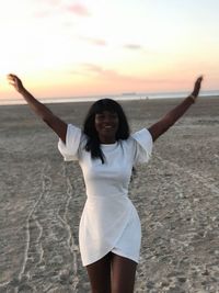 Woman with arms raised standing at beach during sunset