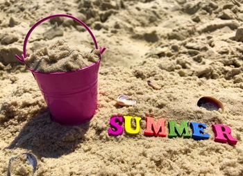 High angle view of colorful text by bucket on sand at beach