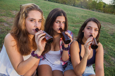 Portrait of young women drinking alcohol while sitting on field