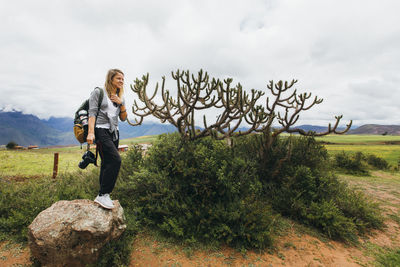 Young woman with a camera is standing on a rock near a cactus in peru