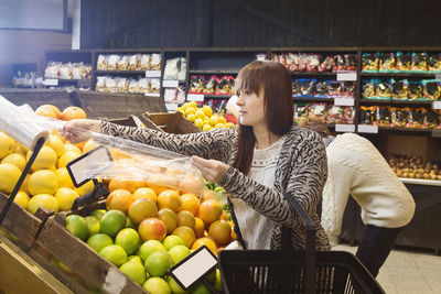 Young woman shopping fruits at supermarket with man in background