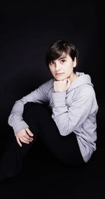 Portrait of young man sitting against black background