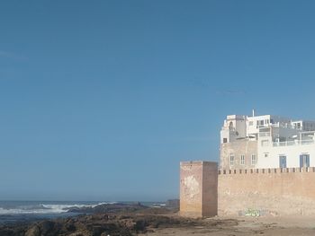 Buildings by sea against clear blue sky