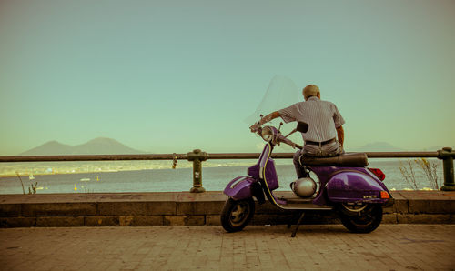 Rear view of man cycling by sea against clear sky