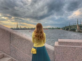 Rear view of woman standing by railing against sky