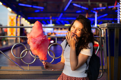Young woman holding ice cream standing at illuminated shop