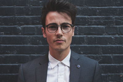 Close-up portrait of young businessman wearing eyeglasses against brick wall