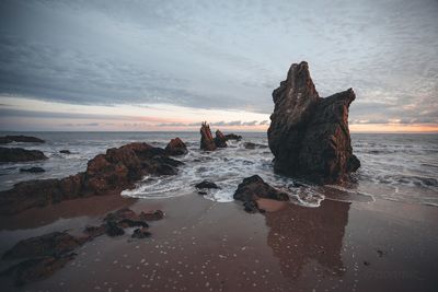 Rock formation on beach against sky during sunset