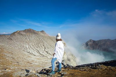 Woman looking at view of hot spring standing on mountain against sky