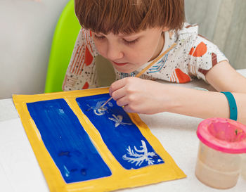 Cute boy painting on paper at home