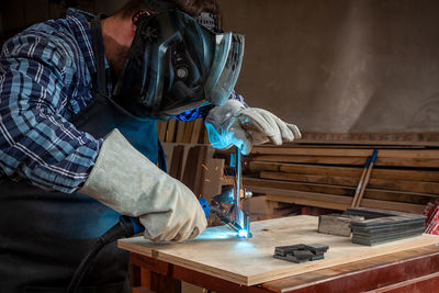 A young man welder in uniform, welding mask and welders leathers, weld metal with a arc welding 