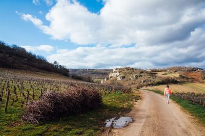 Rear view of woman walking on road amidst land against sky