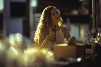 Young woman holding drink while sitting at cafe