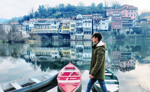 Man walking by boats moored at shore against sky